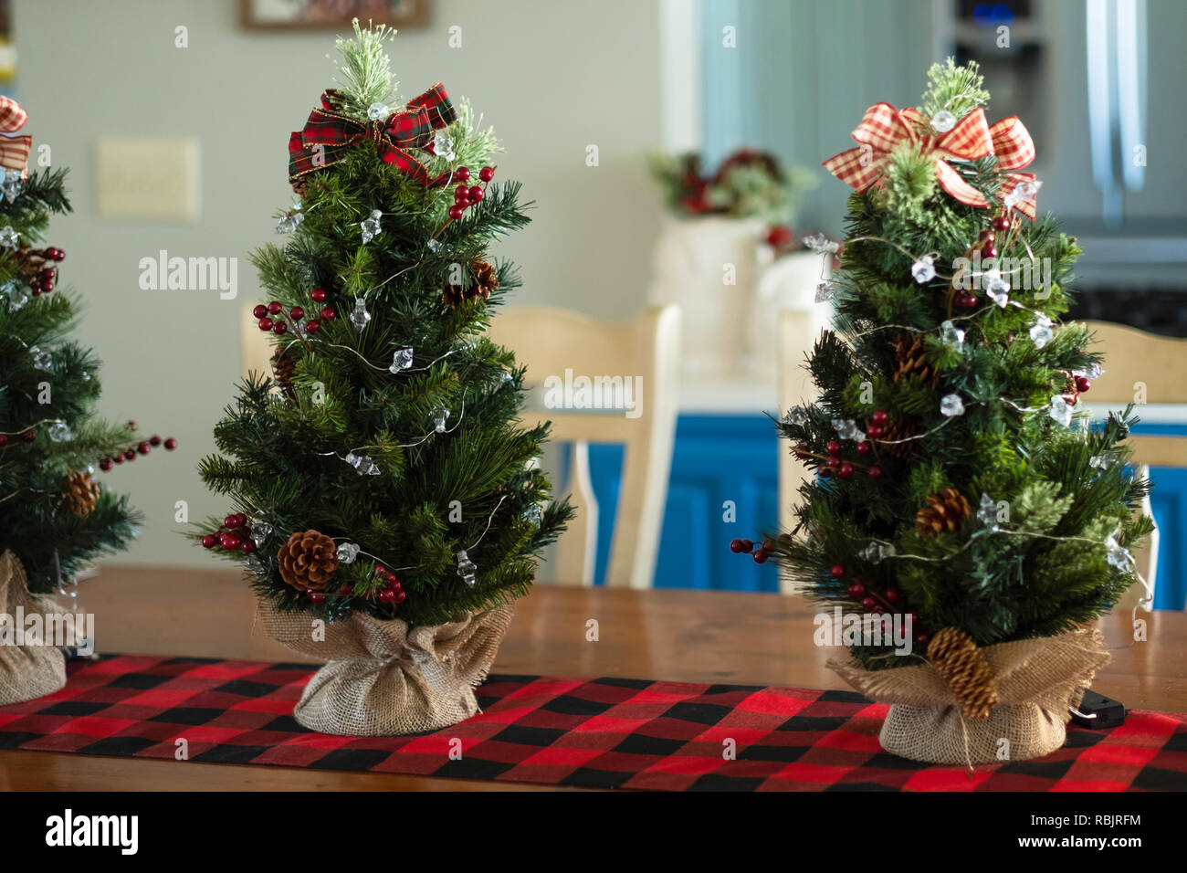 Trois arbres de Noël table miniature avec de la toile de jute sur un chemin de table rouge et noir. Décoration de Noël à l'intérieur. Banque D'Images