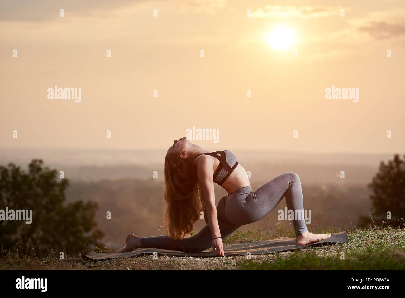 Jolie fille avec de beaux pieds nus slim longs cheveux d'or dans la formation d'été ensemble en posture de yoga compliqué sur misty rose brillant ciel à soleils Banque D'Images