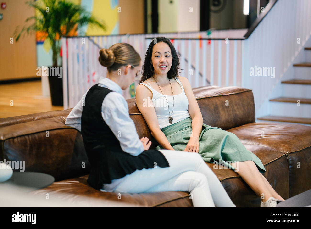 Deux collègues dans un milieu de travail diversifié ont une réunion ensemble sur un canapé dans un bureau à la mode. Une femme est de race blanche et les autres pays asiatiques Banque D'Images