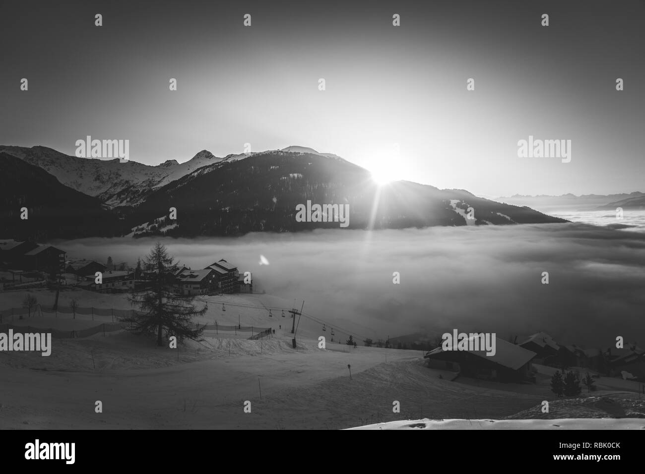 Un noir et blanc du soleil derrière une montagne, avec un lac de nuages au-dessous Banque D'Images