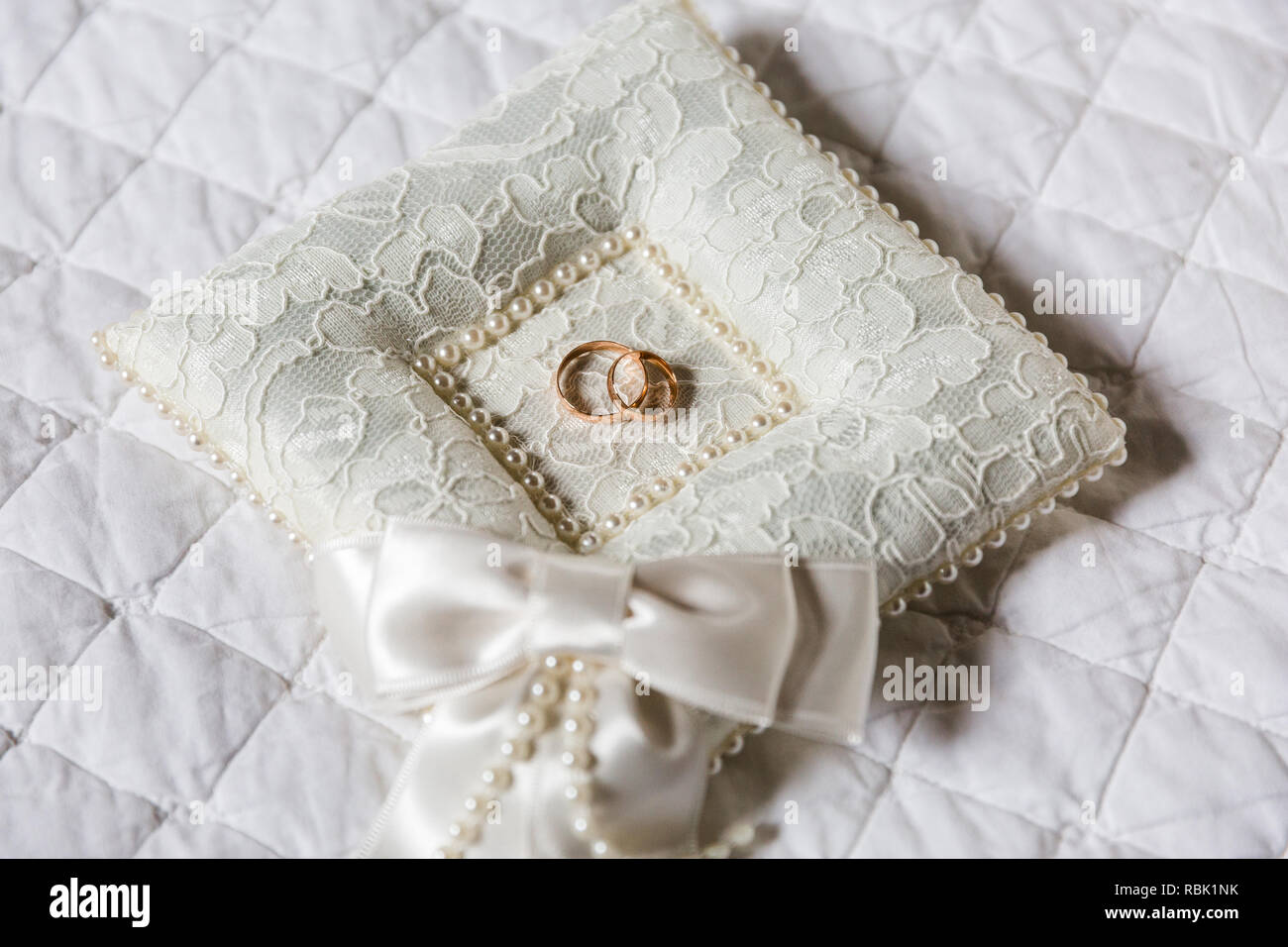 Une paire de bagues de mariage sur un oreiller blanc. L'oreiller a une texture de dentelle, dans le centre de l'oreiller est une cavité dans laquelle les anneaux sont. Banque D'Images