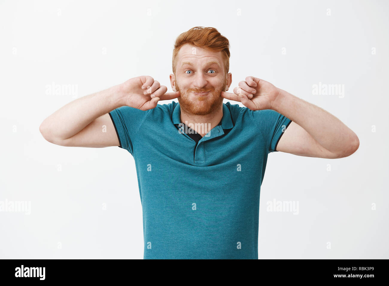 Drôle et heureux papa mature rousse jouant avec fils, souffler vers le haut, apnée et piquer les joues en souriant largement, de jouer et de faire des grimaces sur fond gris Banque D'Images