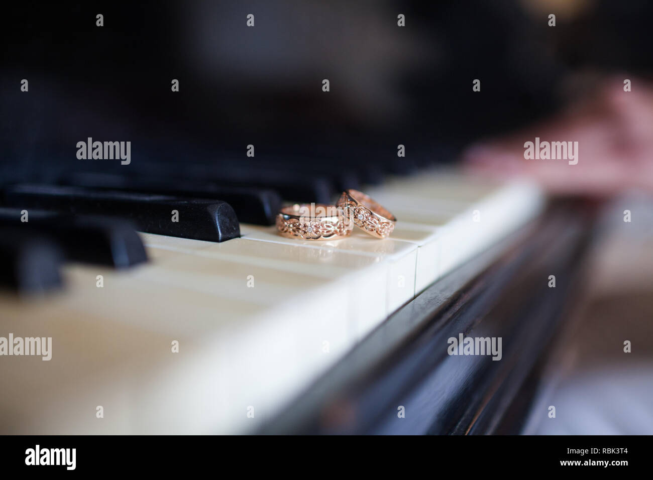 Une paire de bagues de mariage sont sur les touches du piano noir. Dans l'arrière-plan dans la main de femme un flou est discernable, allongé sur les touches. Banque D'Images