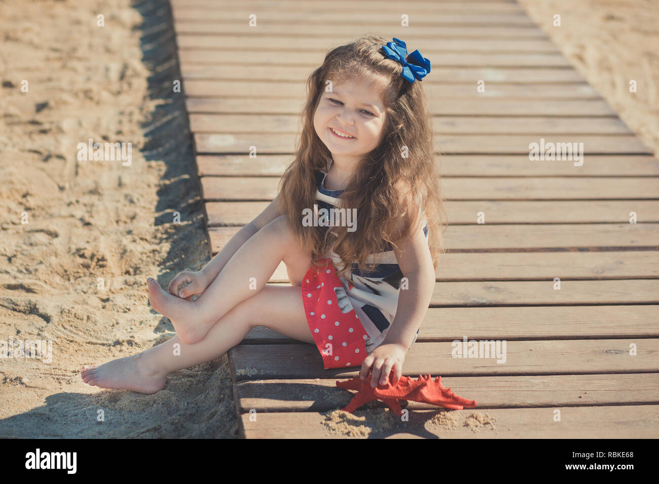 Cute little girl profiter de l'heure d'été sur la plage côté mer  professionnels jouant avec étoile rouge et petite ancre sur le sable jouet  portant des vêtements avec nobby brunette ha Photo
