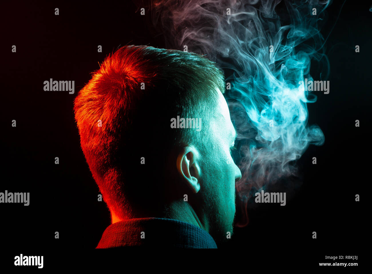 Une vue de l'arrière de la tête d'un gars autour dans un shirt de fumer la vape et exhalant la fumée colorée de vert à différentes parties de lui-même sur un b Banque D'Images