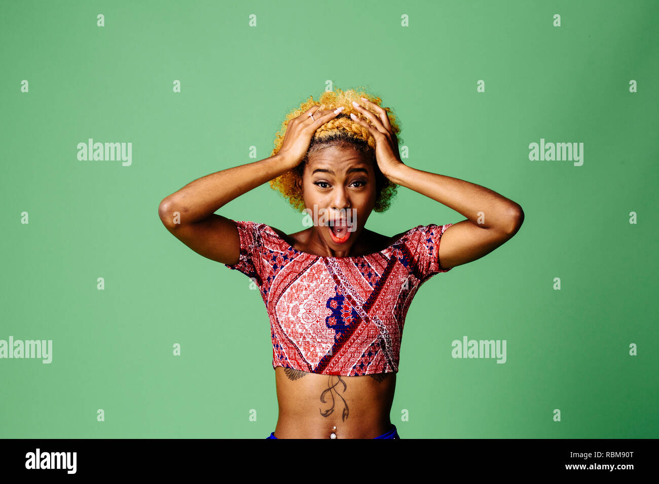 Jeune femme tenant sa tête avec la bouche ouverte dans l'incrédulité et le choc, isolé sur fond vert studio Banque D'Images