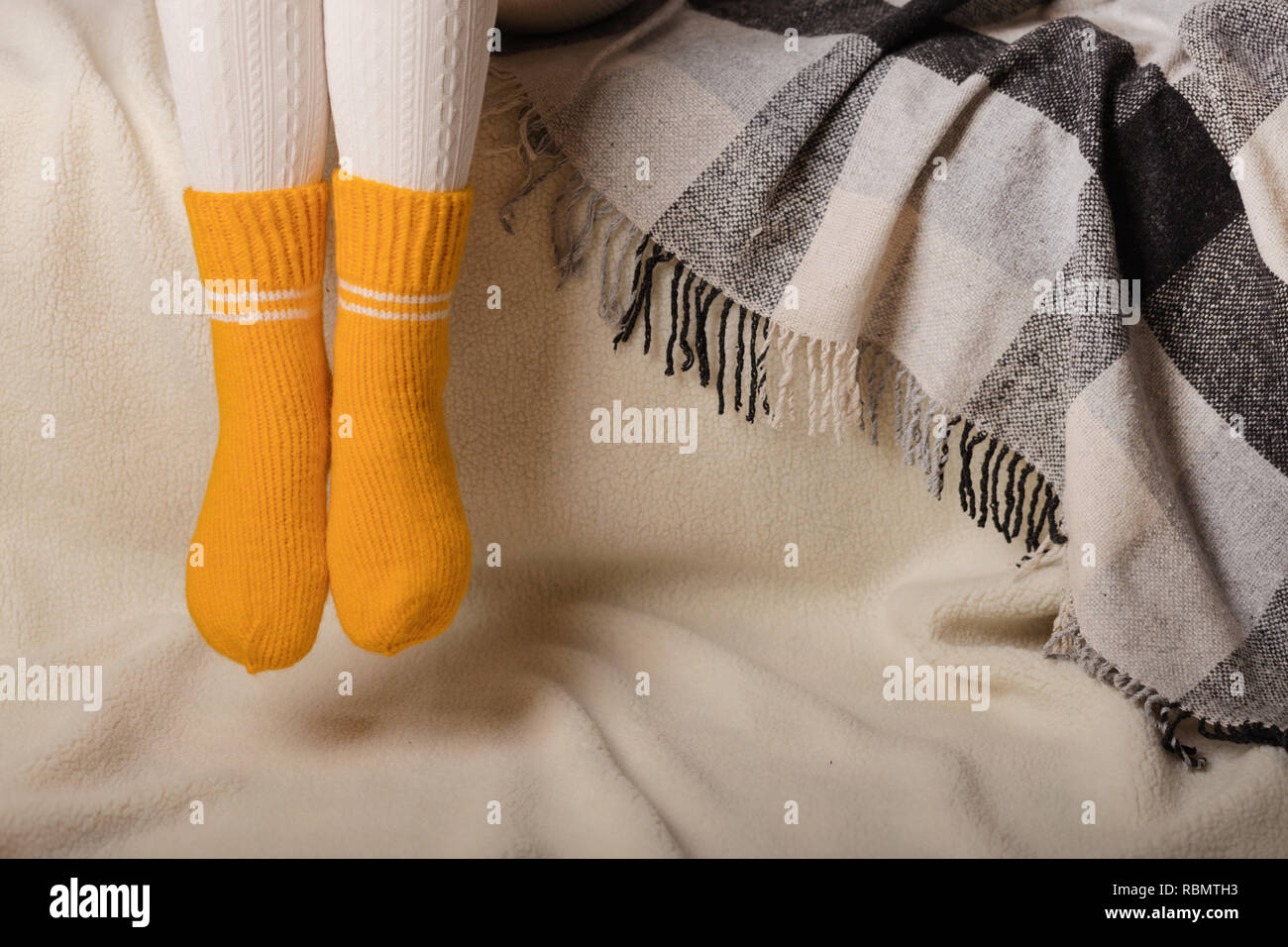 Les jambes des femmes en blanc chaud et collant en tricot chaussettes jaunes sur un fond blanc en fausse fourrure. Banque D'Images