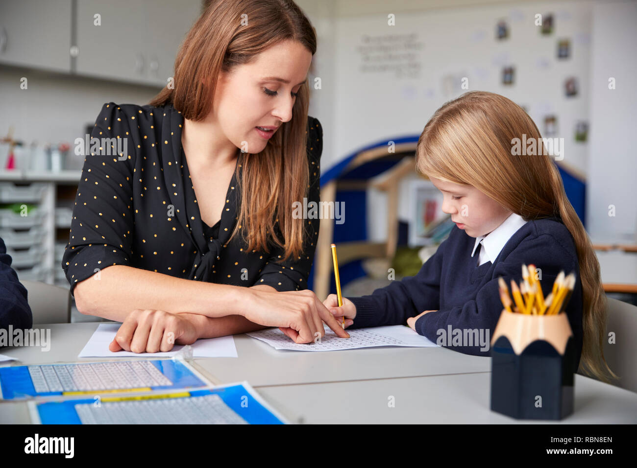 Femme professeur assis à une table dans une salle de classe avec une écolière, l'aider avec son travail, selective focus Banque D'Images