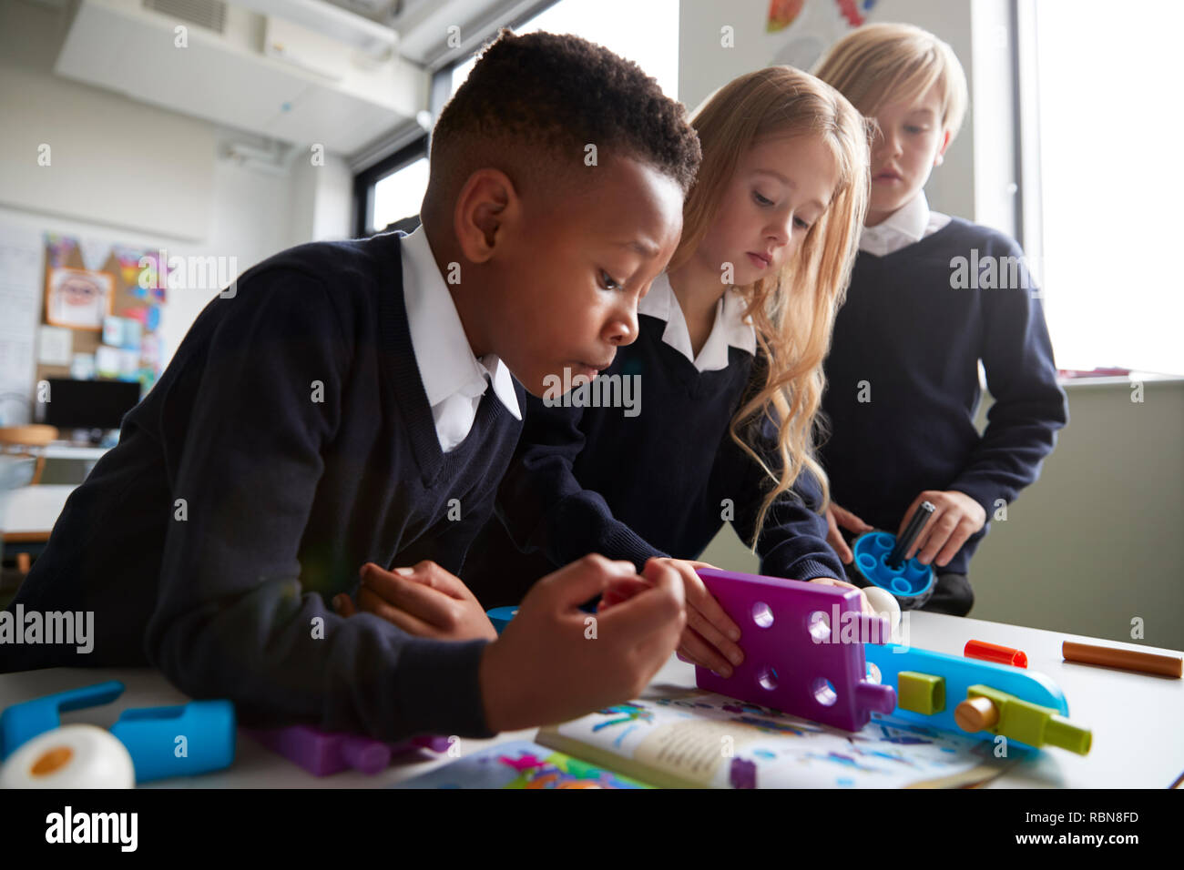 Près de trois enfants de l'école primaire travaillant ensemble avec les blocs de construction de jouets dans une salle de classe, low angle view Banque D'Images
