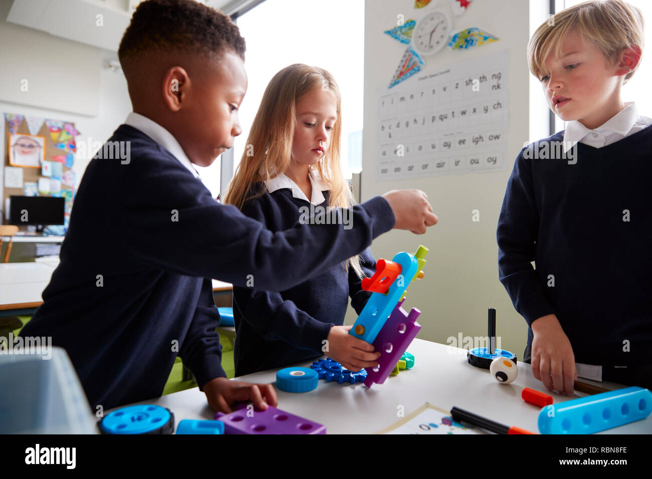 Près de trois enfants de l'école primaire travaillant ensemble avec les blocs de construction de jouets dans une salle de classe, side view Banque D'Images