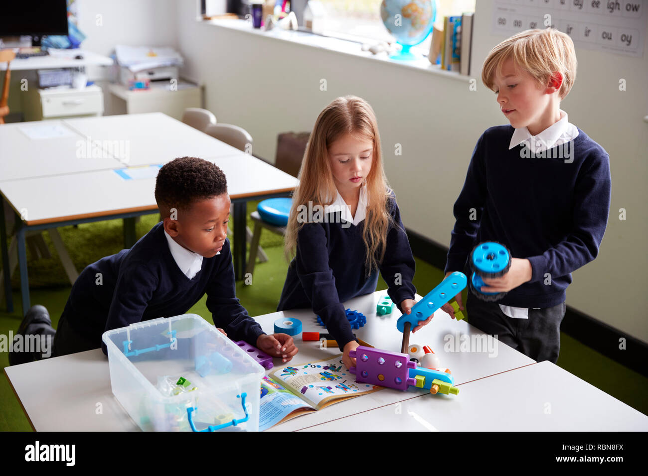 Portrait de trois enfants de l'école primaire debout à une table dans une salle de classe, en collaboration avec les blocs de construction de jouets Banque D'Images