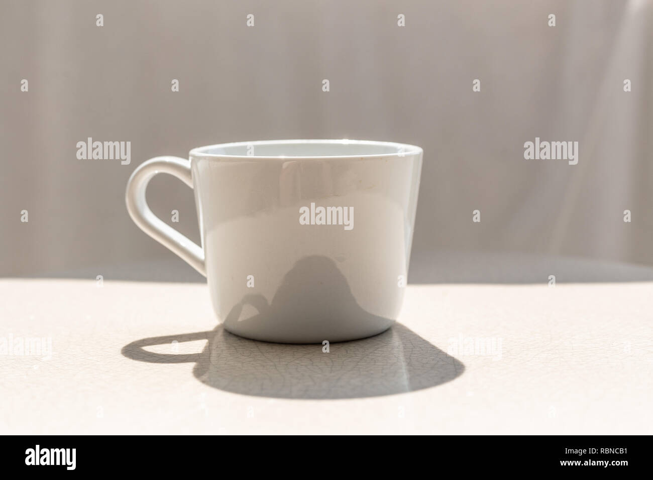 Tasse à café en céramique blanche sur table en céramique blanche, extérieur aux beaux jours avec l'ombre de la coupe sur la table Banque D'Images
