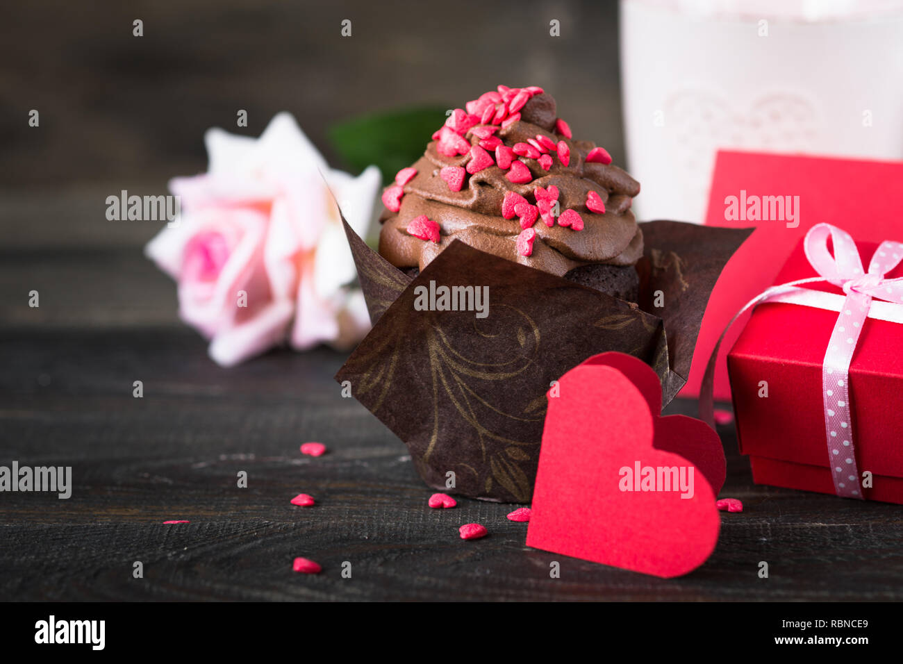 Petit gâteau au chocolat avec crème fouettée, parsemé de coeurs rouges tasse de thé rose cadeau. Valentine's Day background Banque D'Images