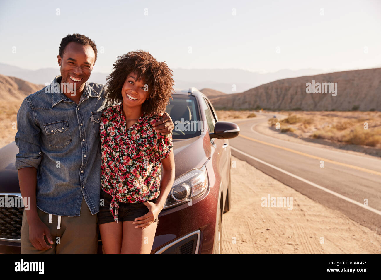 Jeune black couple debout sur leur voiture par la route du désert Banque D'Images Jeune black couple debout sur leur voiture par la route du désert Banque D'Images