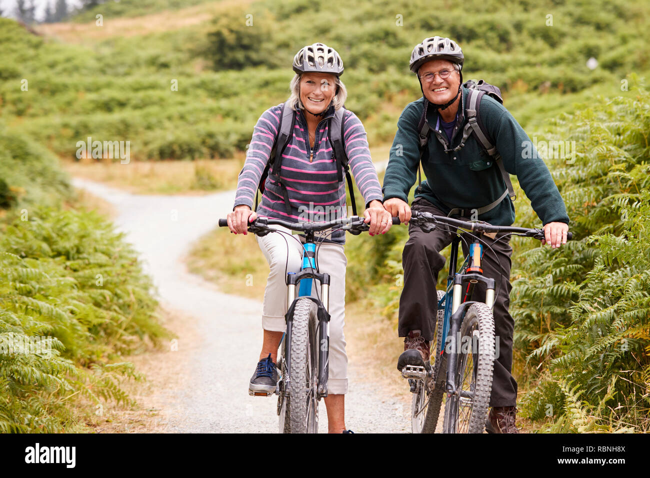 Senior couple sitting on mountain bikes dans un chemin de campagne lors d'une vacances de camping, looking at camera, front view Banque D'Images