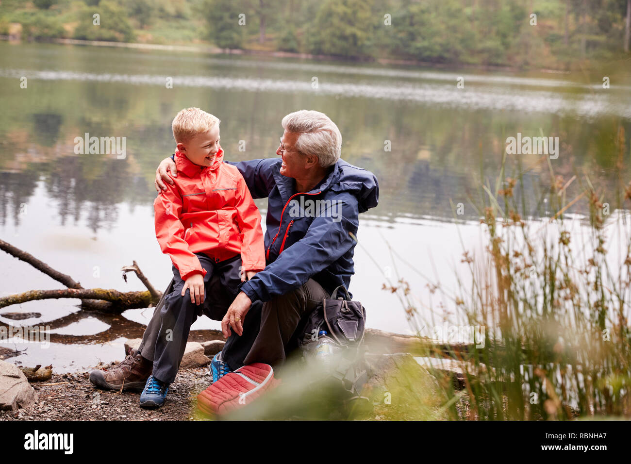 Petit-fils du grand-père assis sur son genou à la rive d'un lac, Lake District, UK Banque D'Images