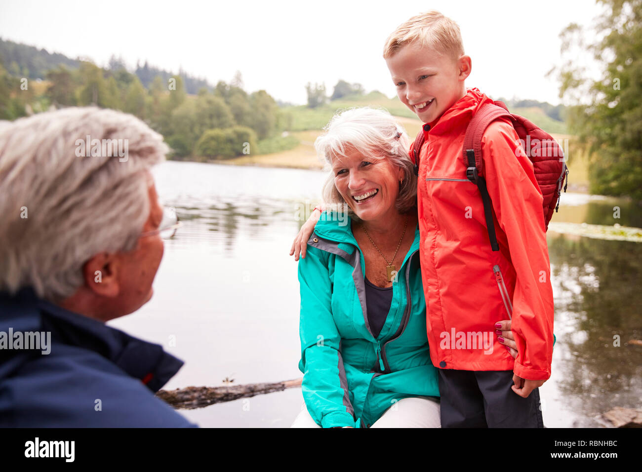 Pré-ado garçon debout à côté de ses grands-parents, assis sur la rive d'un lac, Lake District, UK Banque D'Images