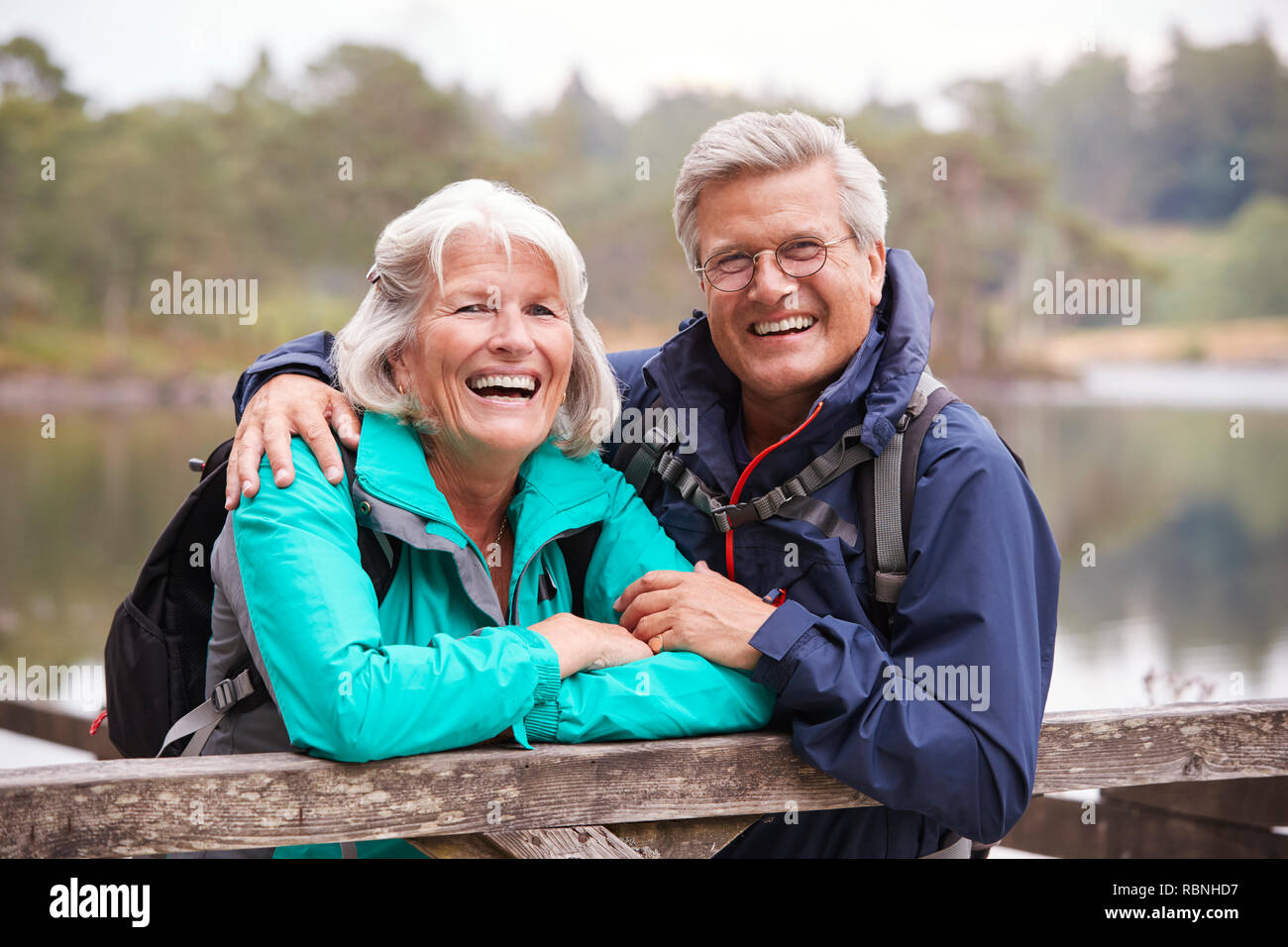 Happy senior couple leaning on une clôture en bois de rire à l'appareil photo, Close up, Lake District, UK Banque D'Images