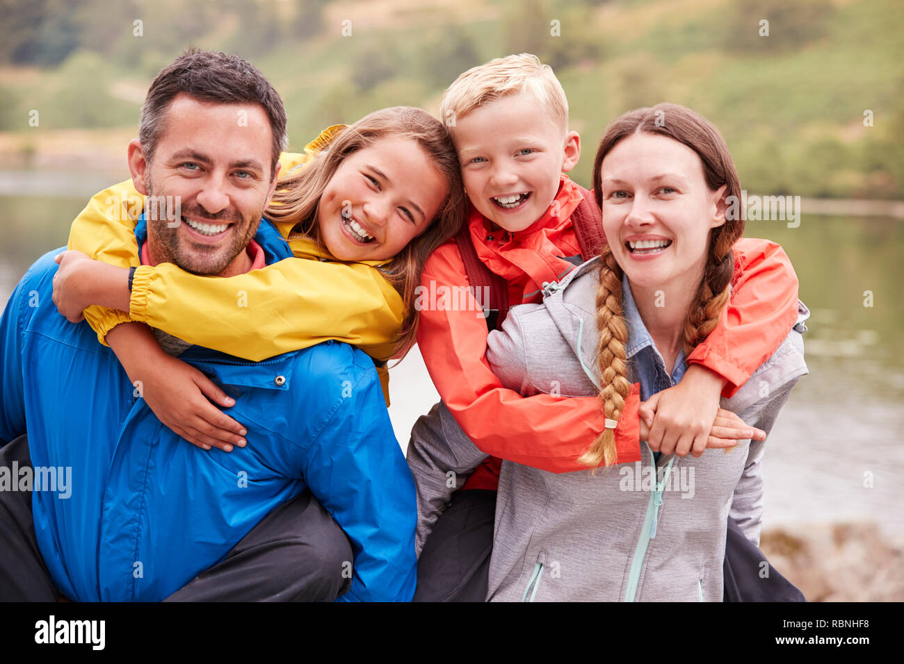 Les parents sur le dos de leurs enfants et de rire à l'appareil photo dans la campagne, Close up, Lake District, UK Banque D'Images
