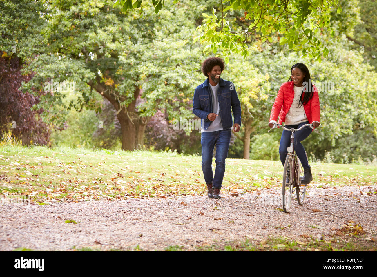 Black couple s'amusant dans un parc, le woman riding a bike, front view Banque D'Images
