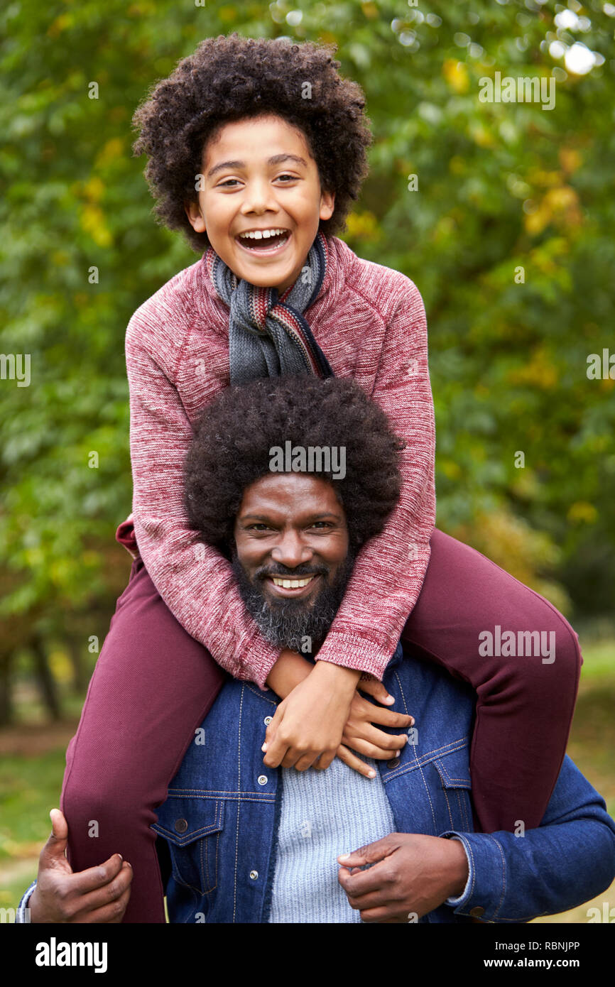 Âge moyen noir homme portant son fils sur ses épaules dans le parc, les deux souriant pour appareil photo, Close up Banque D'Images