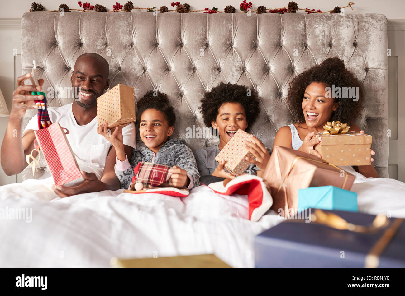 Young mixed race family assis ensemble au lit holding présente le matin de Noël, vue de face, Close up Banque D'Images
