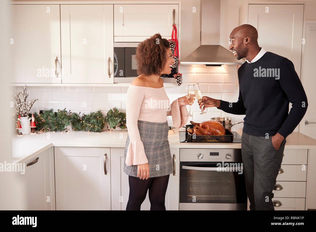 Les jeunes adultes mixed race couple faire un toast au champagne dans la cuisine tout en préparant le dîner de Noël, side view Banque D'Images