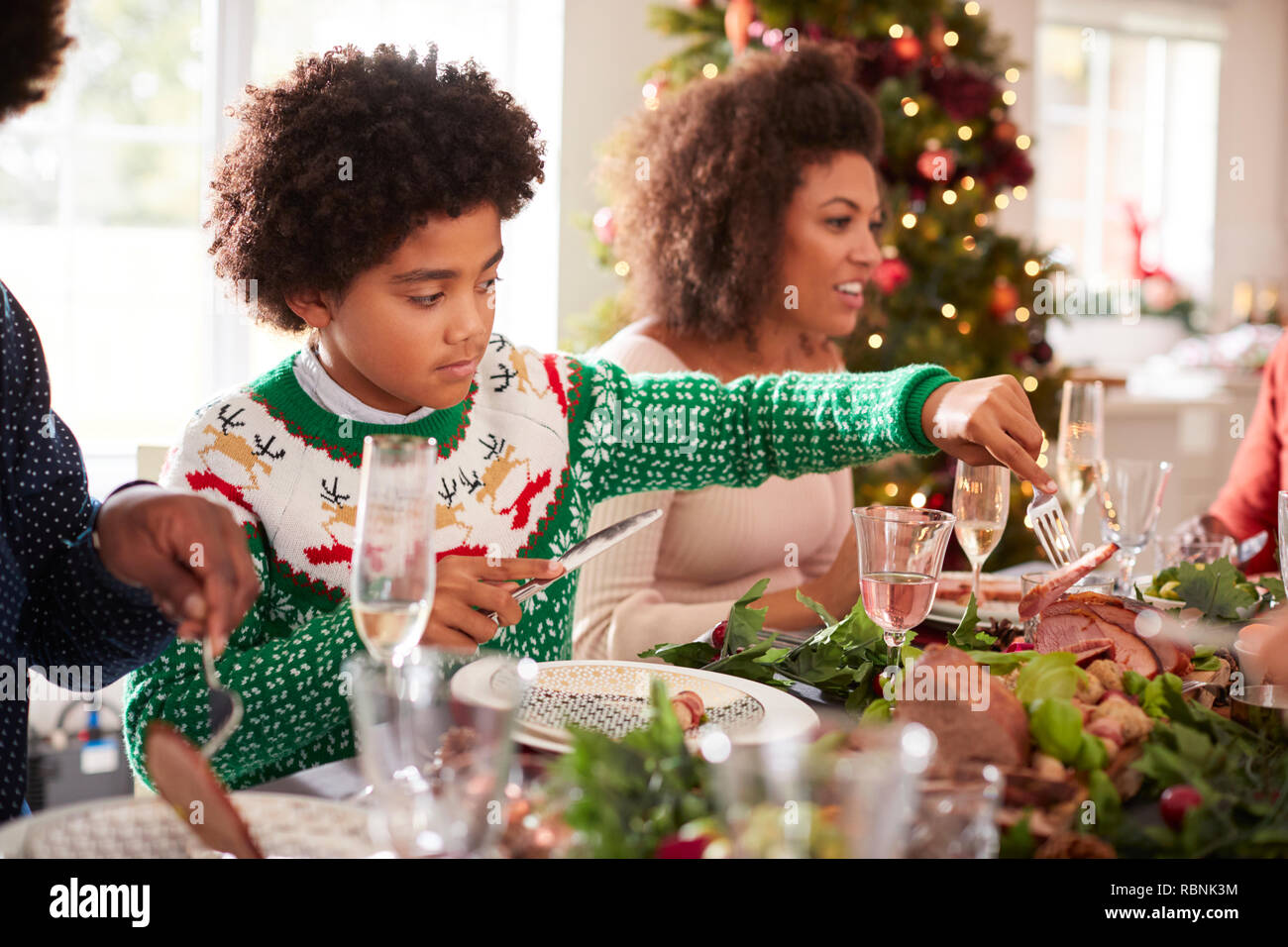 Le Tween garçon noir servant de la dinde rôtie lui-même assis à la table de dîner de Noël avec sa famille, side view Banque D'Images