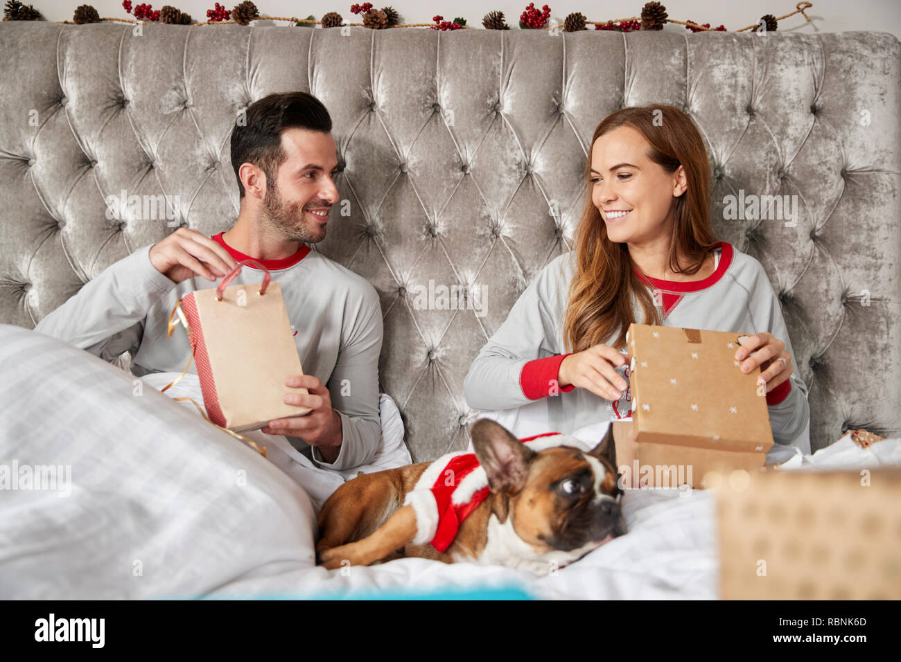 Couple au lit à la maison avec un chien habillé en costume père noël Cadeaux ouverture le jour de Noël Banque D'Images