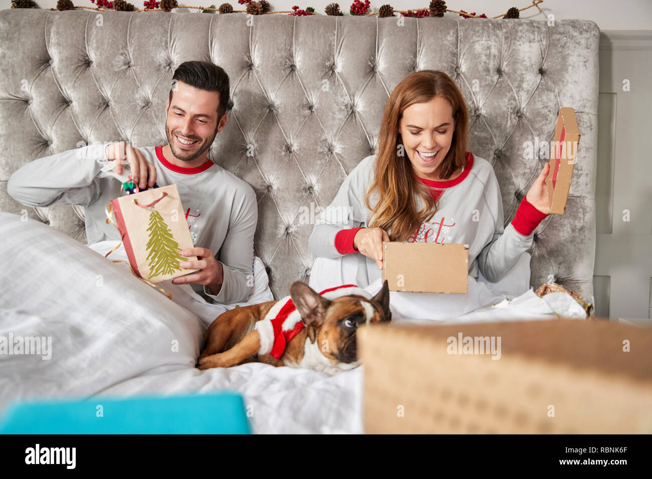 Couple au lit à la maison avec un chien habillé en costume père noël Cadeaux ouverture le jour de Noël Banque D'Images