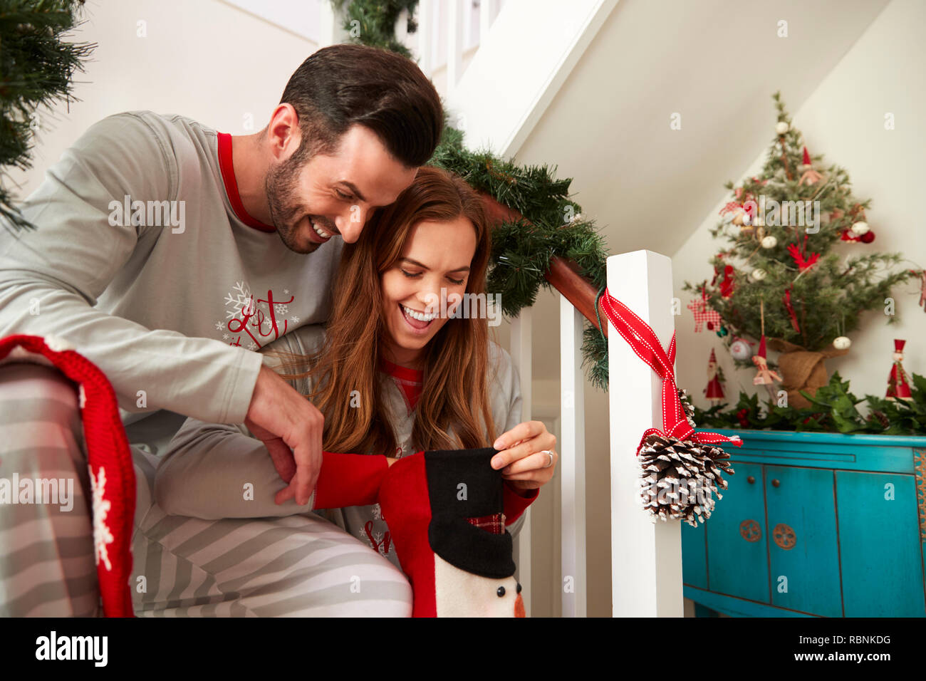 Heureux Couple Wearing Pyjamas assis dans les escaliers à la recherche en bas le matin de Noël Banque D'Images