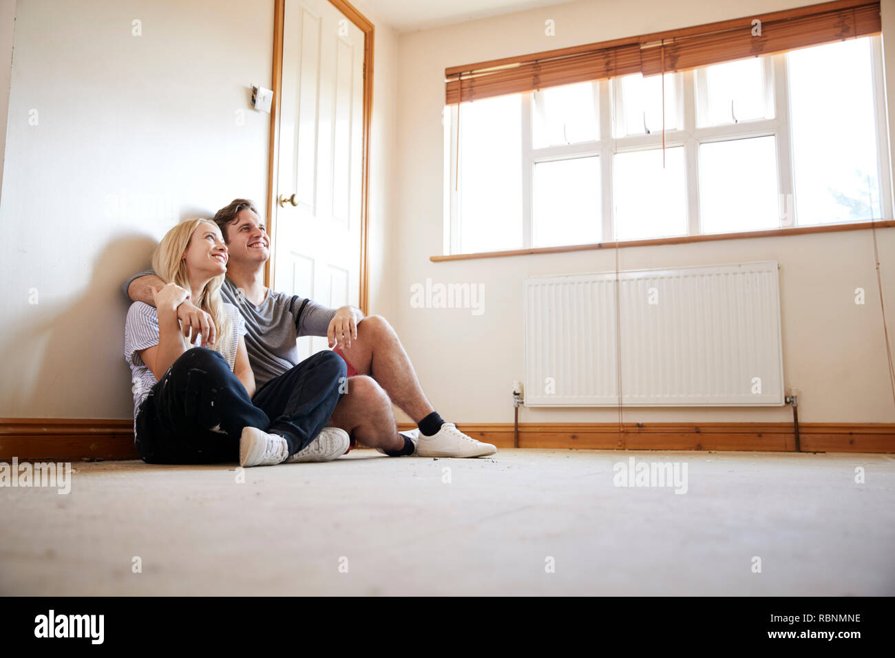 Couple Sitting on Floor In Empty Room de nouvelle conception de la planification d'accueil Banque D'Images