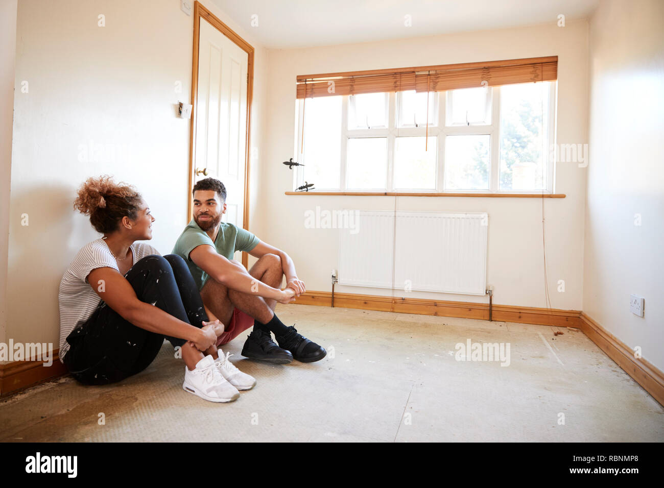 Couple Sitting on Floor In Empty Room de nouvelle conception de la planification d'accueil Banque D'Images