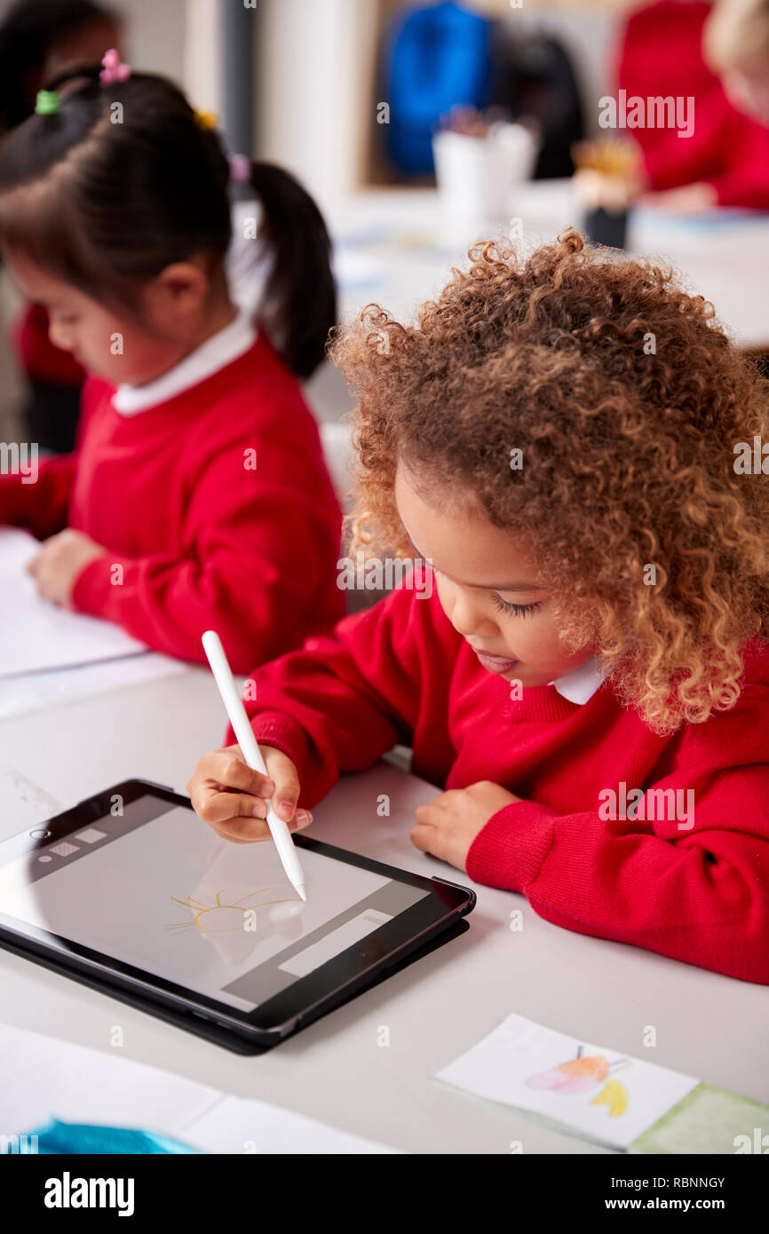 Portrait de jeune écolière portant l'uniforme scolaire assis à 24 dans une petite école de classe à l'aide d'un ordinateur tablette et stylet, Close up, vertical Banque D'Images