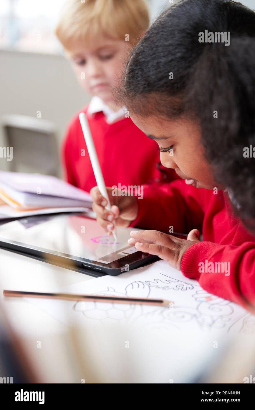 Gros plan d'une lycéenne assise à 24 côté d'un garçon dans une petite école de classe, à l'aide d'un ordinateur tablette et stylet, selective focus, vertical Banque D'Images