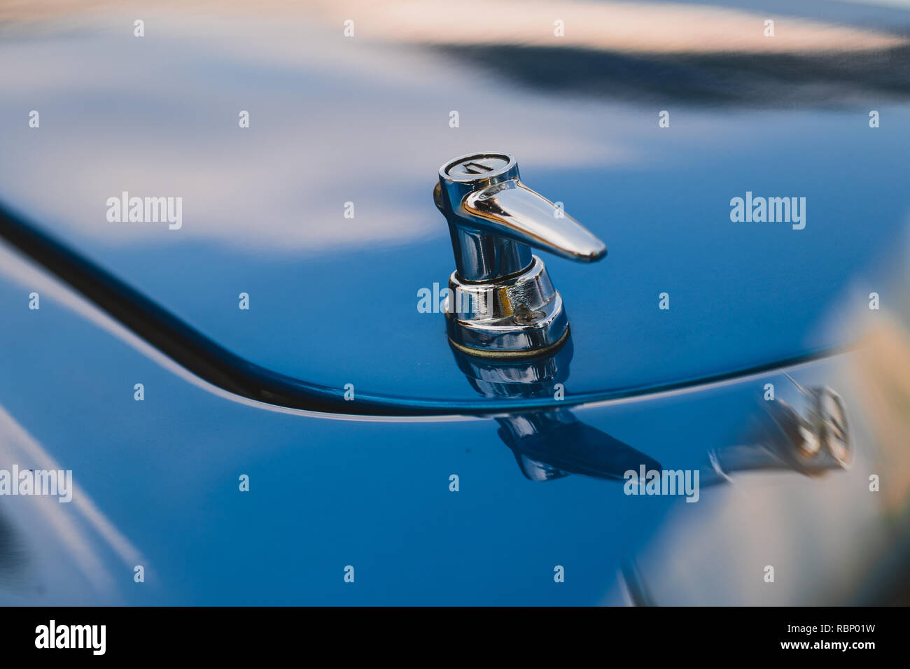 Détail de verrou de capot chrome blue vintage sports car avec la réflexion du ciel dans corps de voiture en arrière-plan. Banque D'Images