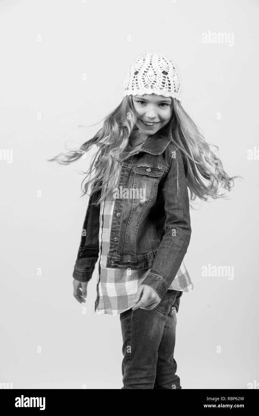 Jeune fille en jeans costume, chapeau, chemise à carreaux sur fond orange. Enfance heureuse concept. La mode, le style, tendance. Beauté, look, coiffure. Modèle enfant sourire avec de longs cheveux blonds Banque D'Images