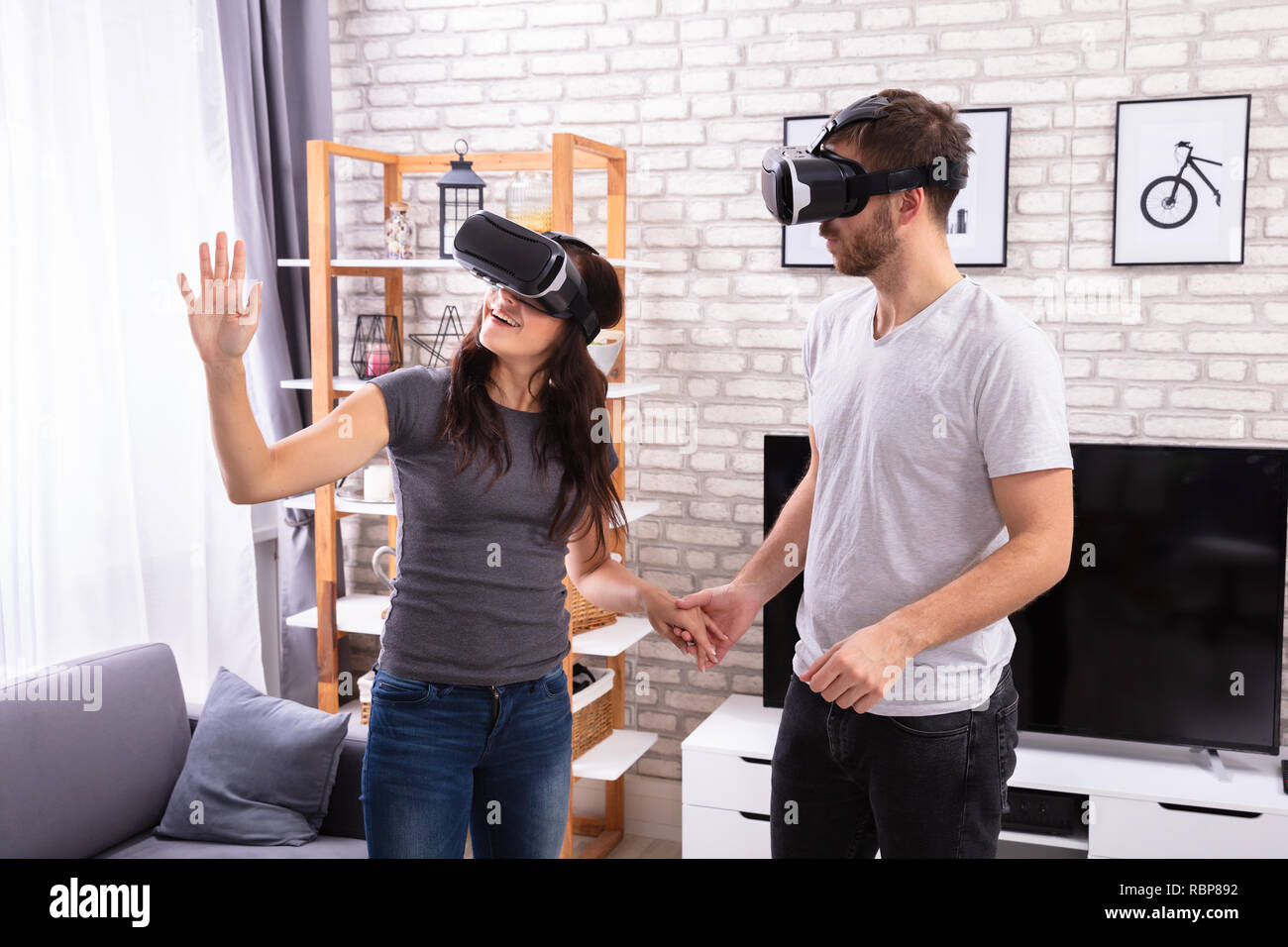 Jeune couple à l'aide de périphériques de réalité virtuelle à la maison Banque D'Images