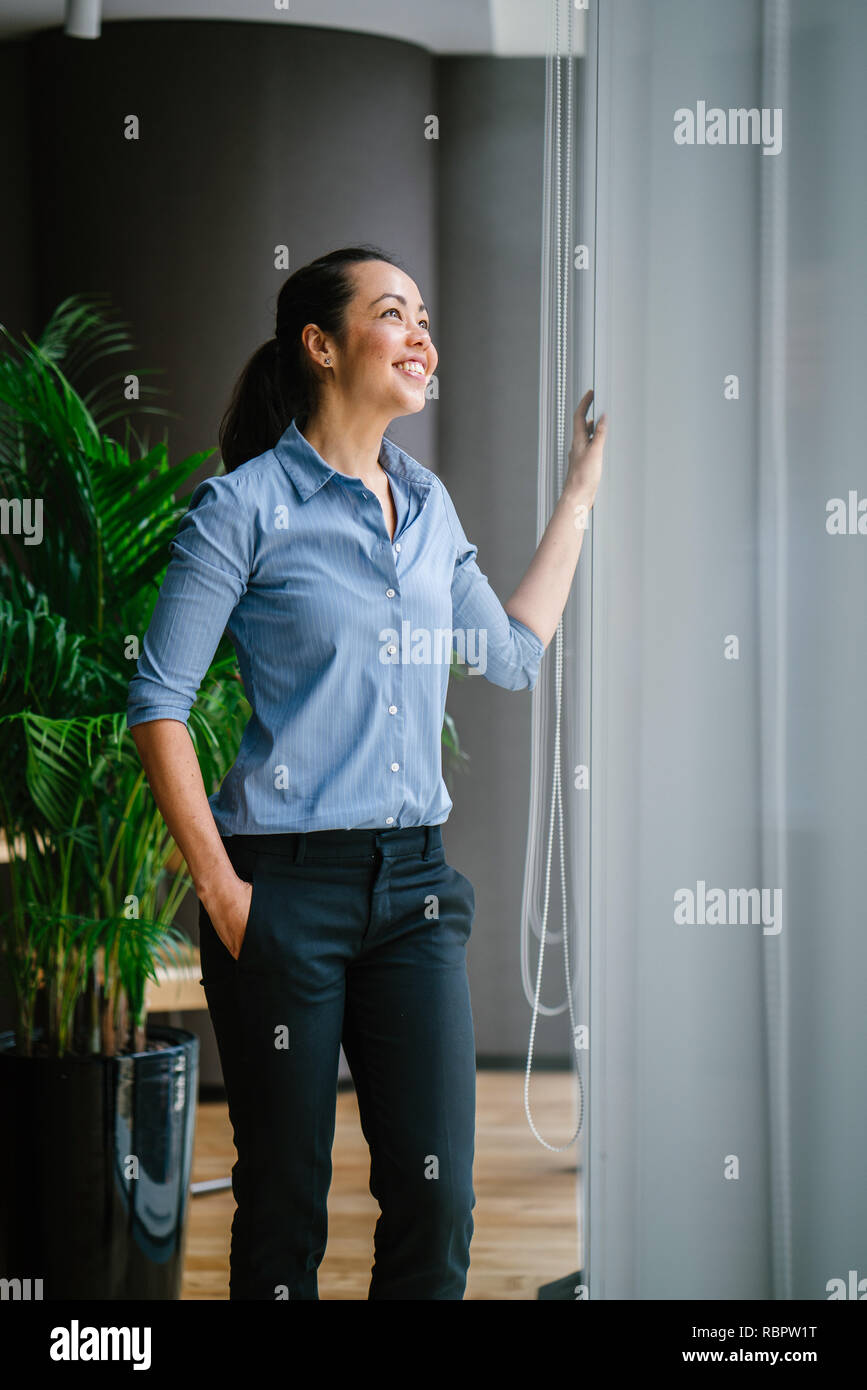 Portrait d'une jolie femme asiatique professionnel dans une chemise et  pantalon debout près de la fenêtre dans son bureau pendant la journée. Elle  sourit joyeusement Photo Stock - Alamy