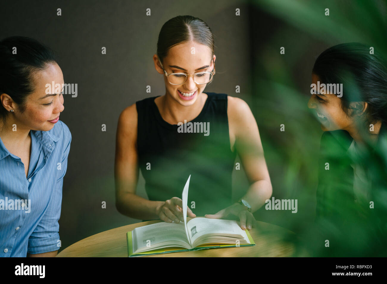 3 jeunes femmes d'origine ethnique différente s'asseoir autour d'une table dans une salle de réunion. Ils sont souriants et bavardant comme ils ont lu un livre. Banque D'Images