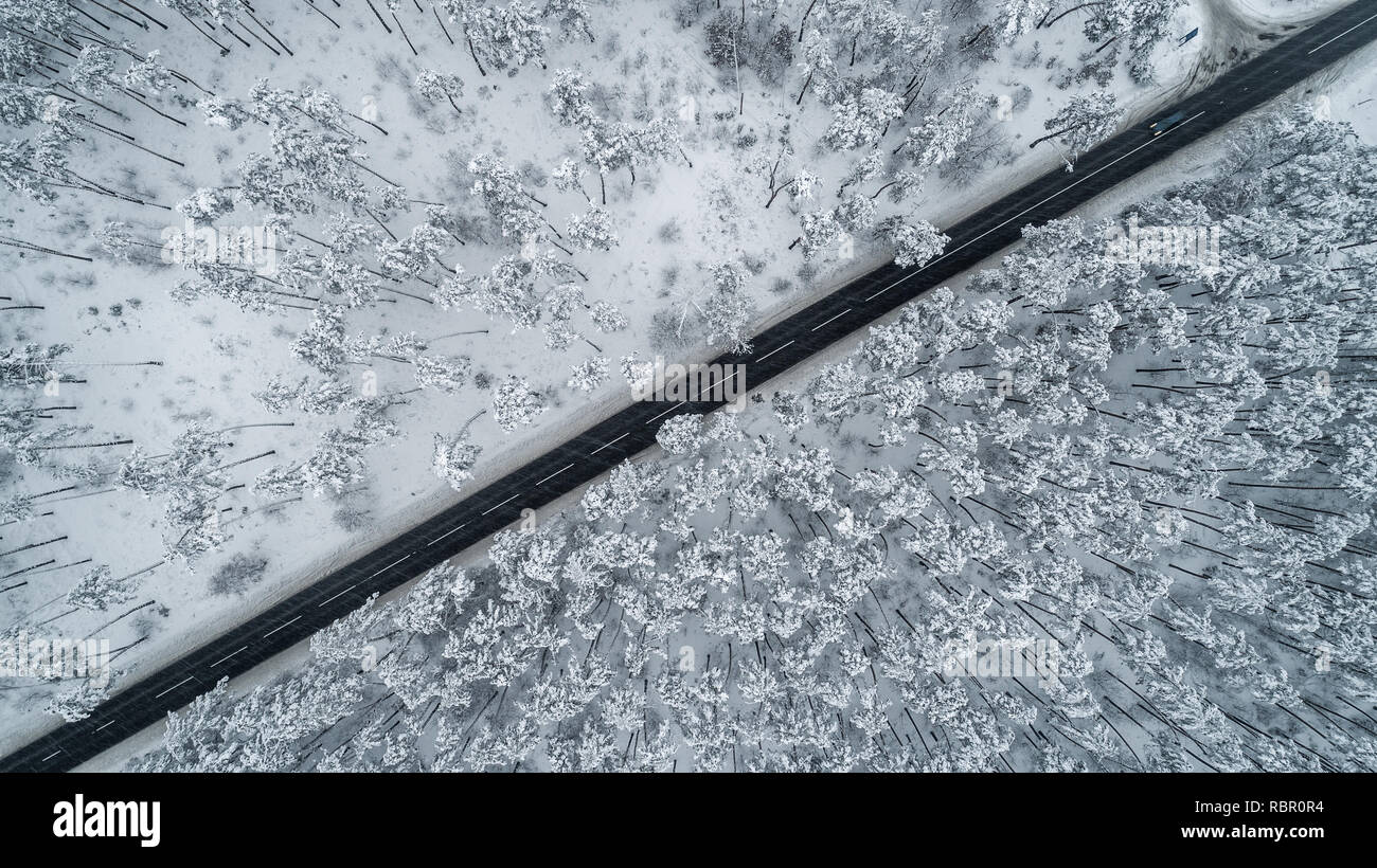 Vue aérienne de la route romantique en passant par la forêt d'hiver couverte de neige. Une vue du haut des pins et une bande noire d'asphalte roa Banque D'Images