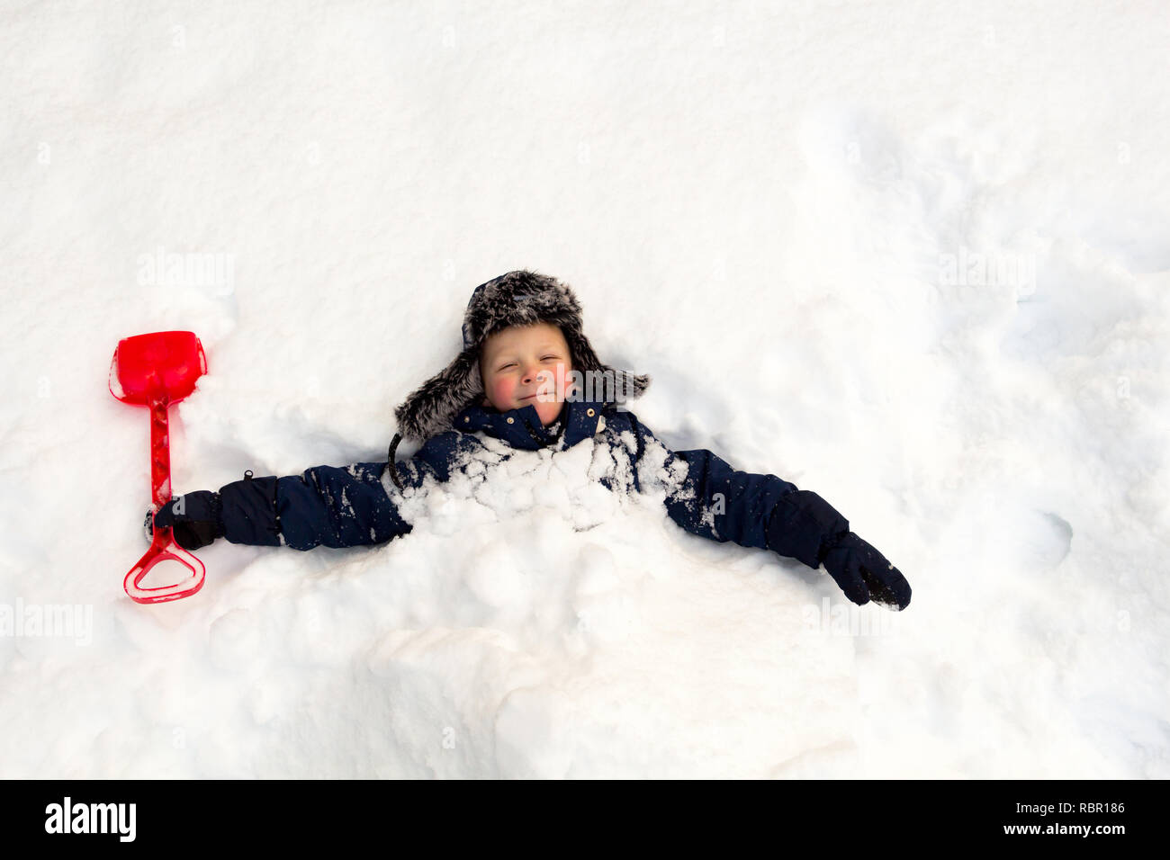 Journée d'hiver, beaucoup de neige, l'enfant enterré lui-même avec une pelle pour enfants autour du cou dans la neige. Banque D'Images
