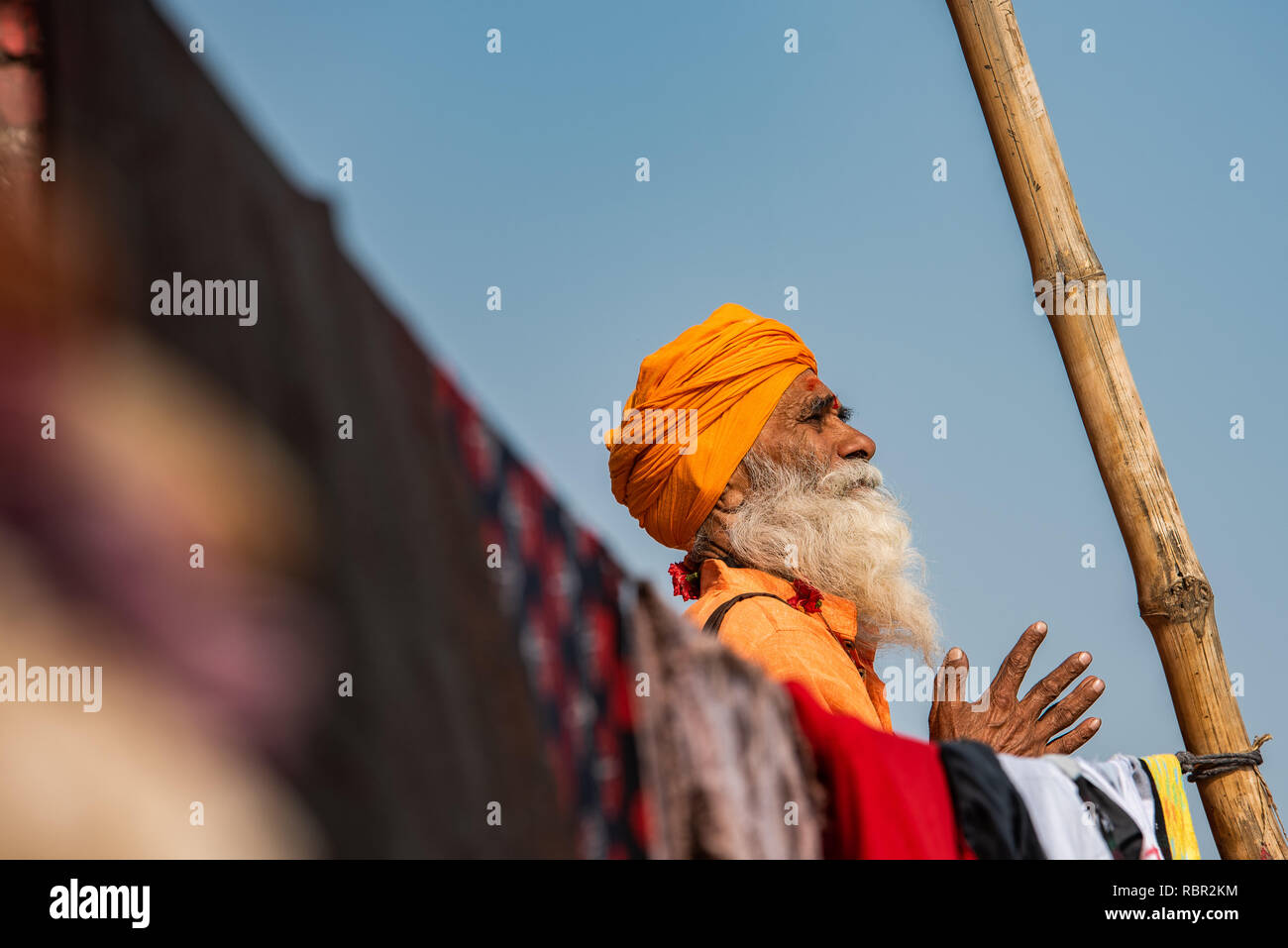 Un saint homme en prière avec ses mains repliées encadrée par un poteau et vêtements en ligne à Varanasi, Inde Banque D'Images