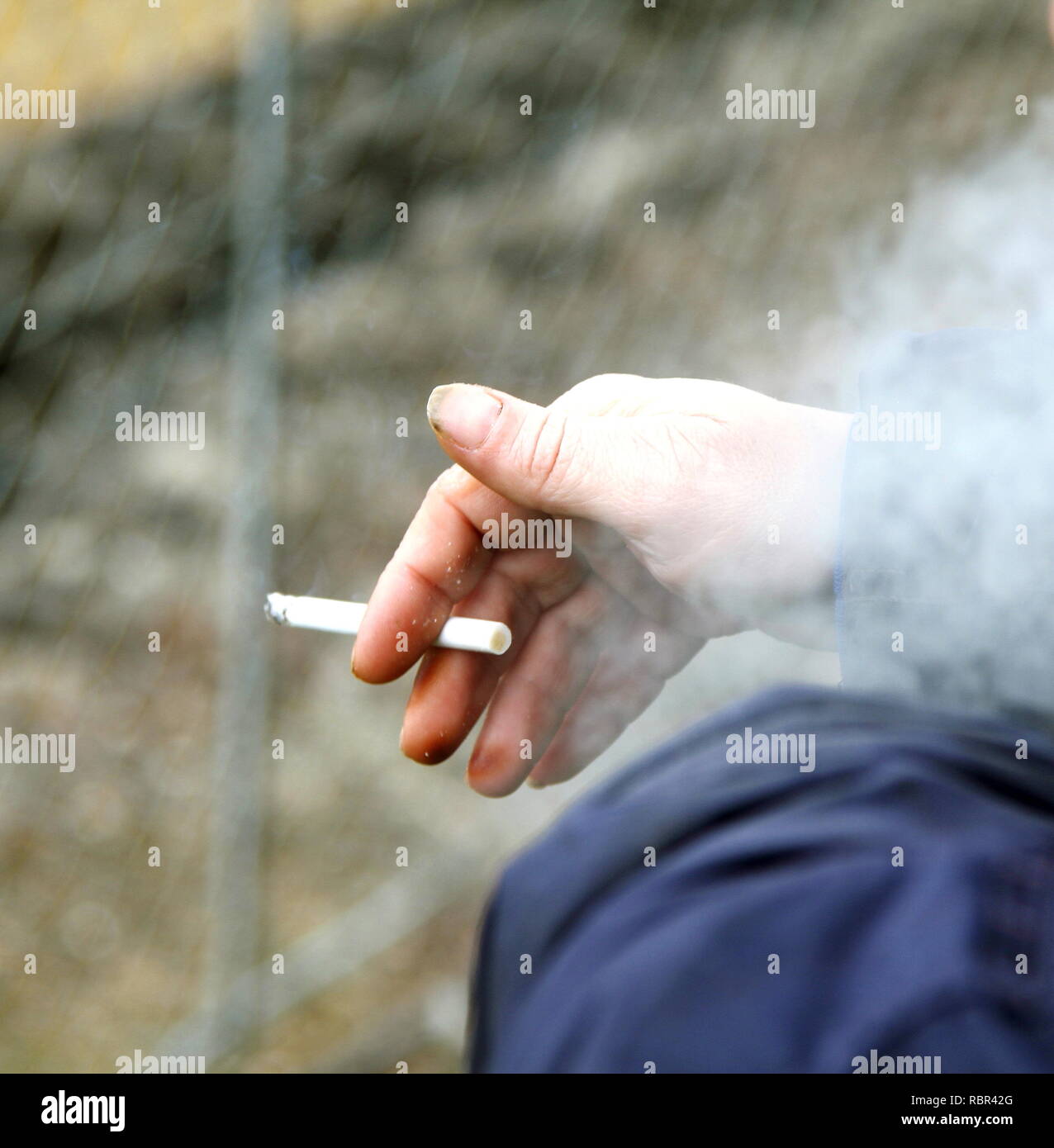 .Fumer une cigarette tenue dans la main droite d'un homme avec des taches de nicotine et de la fumée s'envolent dans l'air. Une dépendance de la cigarette. Le tabac tue arrêter maintenant. Les cigarettes sont coûteux et peut causer de nombreuses maladies. Maladies liées au tabagisme sont bien connus. La dépendance. Banque D'Images