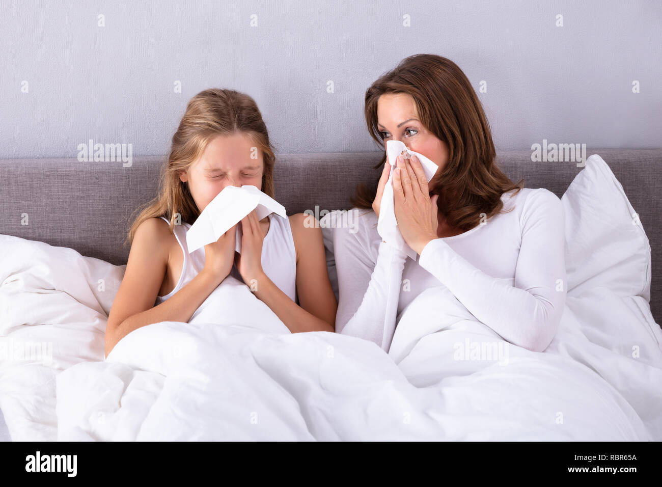 Mère et fille souffrant de soufflage froid son nez avec un mouchoir sur le lit Banque D'Images