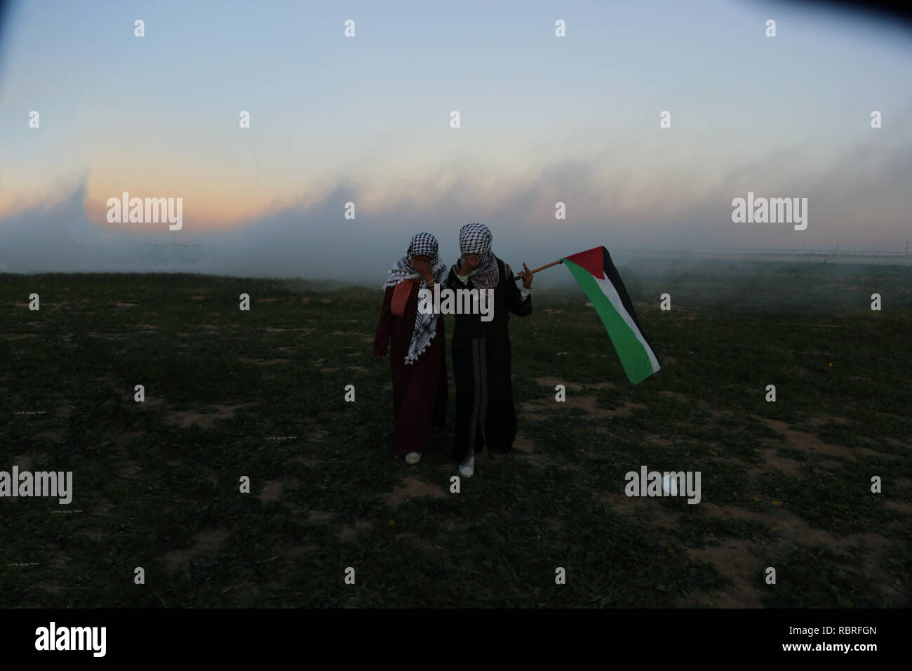 Des manifestants sont vu tenant un drapeau palestinien au milieu des gaz lacrymogènes fumigènes autour d'eux pendant la manifestation. Les Palestiniens se sont affrontés avec les forces israéliennes au cours des manifestations sur le mur entre Gaza et Israël à l'est de Khan Yunis. Banque D'Images