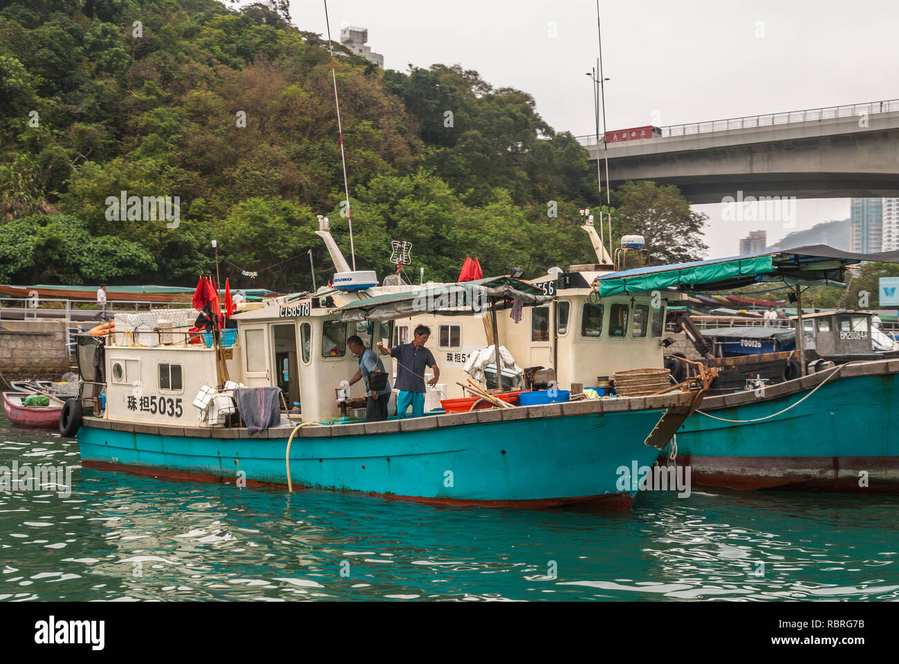 Hong Kong, Chine - 12 mai 2010 : petit bateau de pêche dans le port. D'autres navires amarrés autour. Deux hommes la préparation du navire. La végétation verte Banque D'Images