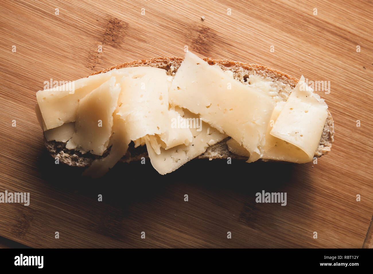Sandwich avec du beurre et du fromage dur sur une tranche de pain de seigle fraîchement cuits sur une planche à découper en bois Banque D'Images