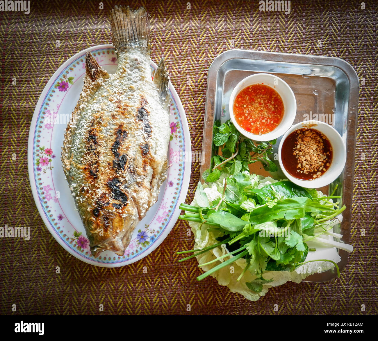 Grillades de Poisson tilapia Tilapia grillé à l'Cook / sur la plaque de sel alimentaire style asiatique avec la sauce et des légumes frais - poissons tilapia thaïlandais brûler herbes brûlées Banque D'Images