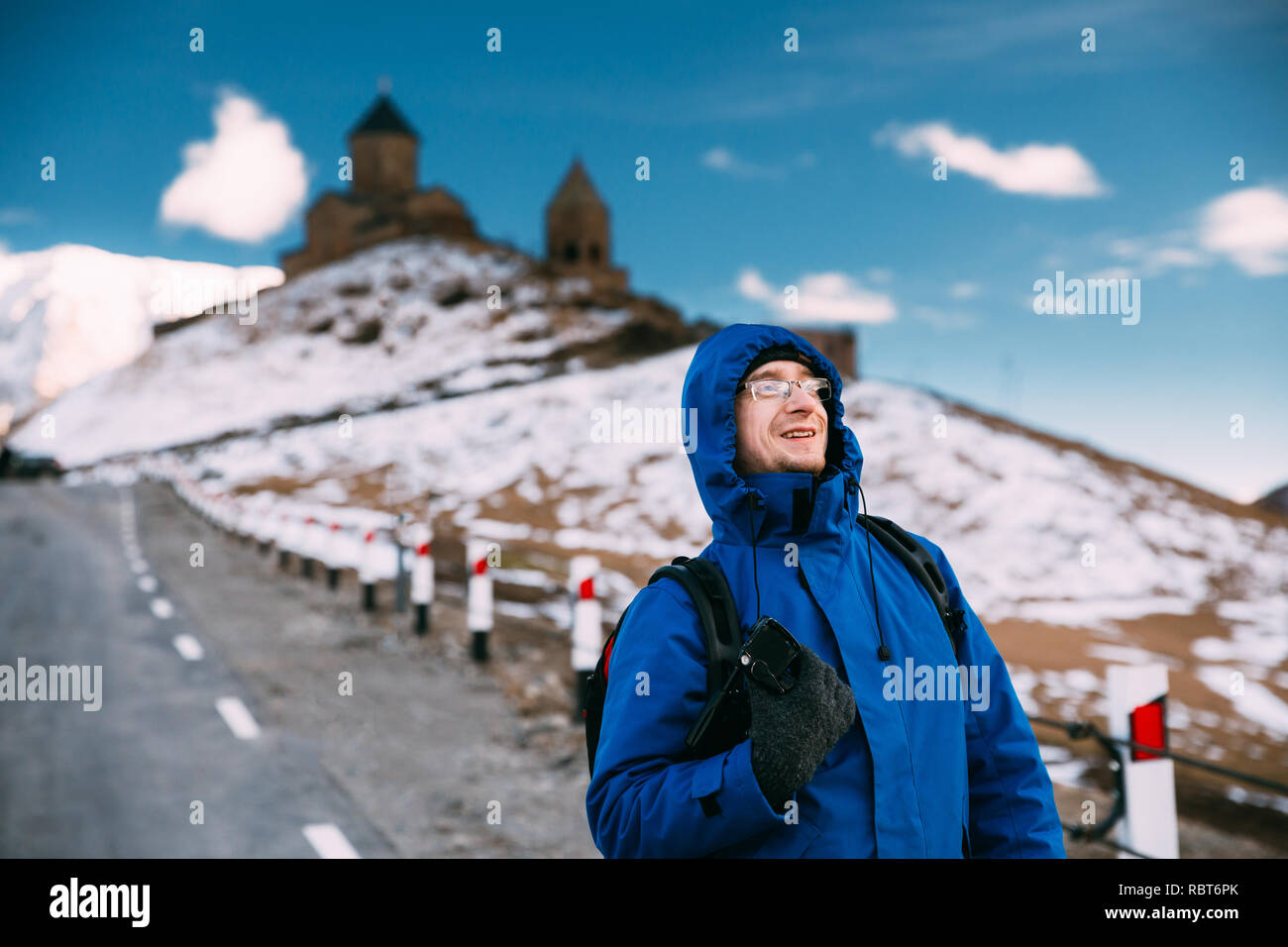 Stepantsminda Gergeti, Géorgie). Photographe Voyageur Backpacker touristiques homme posant près de l'église Holy Trinity - Tsminda Sameba. Belle Lan Géorgienne Banque D'Images